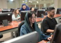 Young woman with scarf over head sitting next to man, using computers in technology suite in higher education institution and concentrating