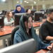 Young woman with scarf over head sitting next to man, using computers in technology suite in higher education institution and concentrating
